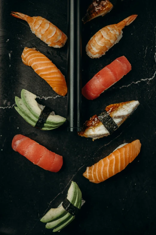 a black plate topped with sushi and chopsticks, by Niko Henrichon, daily specials, 6 pack, marbled, flatlay