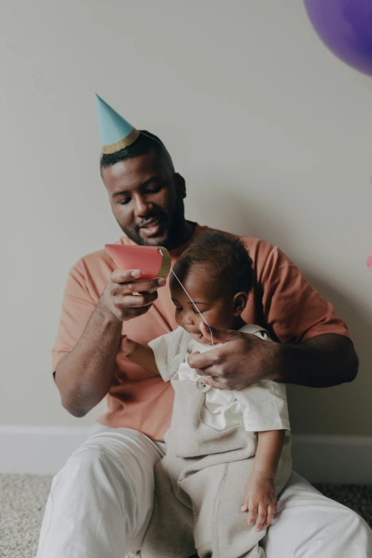 a man sitting on the floor holding a baby, by Adam Saks, pexels contest winner, pals have a birthday party, frank ocean, on grey background, color footage