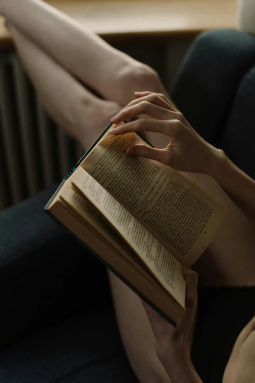 a woman sitting on a couch reading a book, by Adam Marczyński, pexels contest winner, renaissance, sitting on man's fingertip, ( low key light ), ignant, ultra realistic