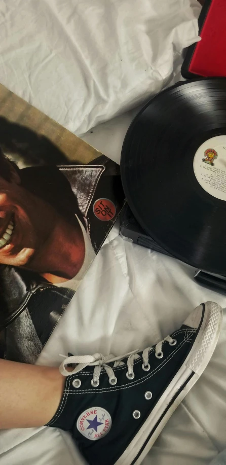 a magazine laying on top of a bed next to a pair of sneakers, an album cover, by Everett Warner, freddie mercury smiling, closeup - view, ap art, soft vinyl