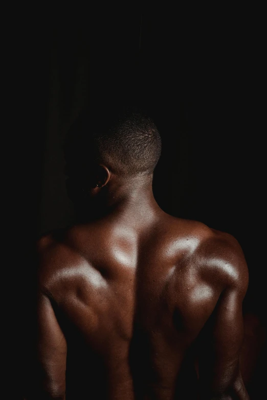 a man standing in the dark with his back turned, an album cover, by Jessie Alexandra Dick, pexels contest winner, renaissance, bare bodybuilder shoulders. kohl, black teenage boy, 30 year old man :: athletic, brown skinned