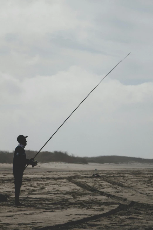 a man standing on a beach holding a fishing pole, from a distance