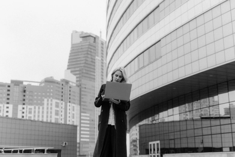 a black and white photo of a woman holding a laptop, a black and white photo, highrise business district, moleksandra shchaslyva, low quality photo, outside on the ground