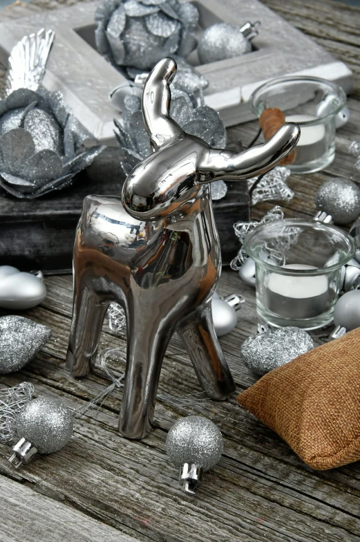 a silver reindeer figurine sitting on top of a wooden table, inspired by Rudolph F. Ingerle, high gloss, molten, various sizes, reflecting