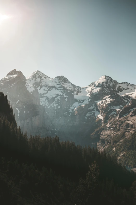 a mountain range with snow covered mountains in the background, by Johannes Voss, pexels contest winner, modernism, trees and cliffs, cinematic morning light, 4 k cinematic panoramic view, clear skies