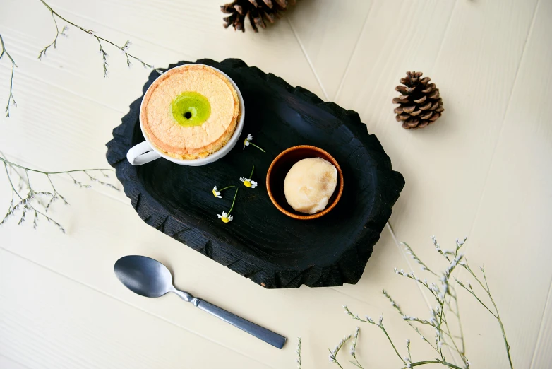 a table topped with a bowl of food and a spoon, inspired by Wlodzimierz Tetmajer, unsplash, bog oak, pastry, panel of black, woodland location