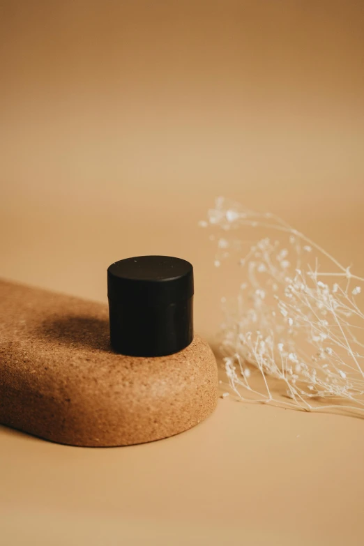 a bottle of perfume sitting on top of a wooden base, unsplash, minimalism, wrapped in black, silicone cover, manuka, small in size