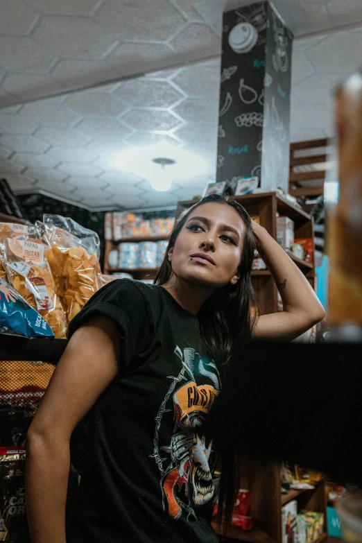 a woman leaning on a shelf in a store, a portrait, trending on unsplash, graffiti, wearing a black shirt, long coffee brown hair, band merchandise, young himalayan woman