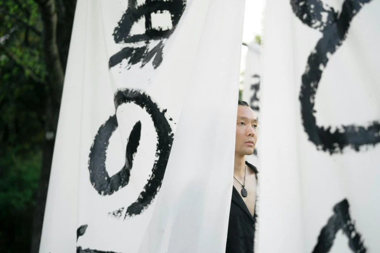 a woman standing in front of a banner with chinese writing on it, inspired by Taro Yamamoto, unsplash, shin hanga, photo of a man, cloth banners, ignant, ethnicity : japanese