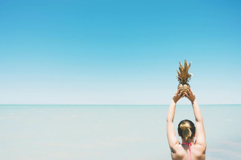 a woman holding a pineapple above her head, pexels contest winner, minimalism, beach setting, tv still, blue sky, viewed from the ocean