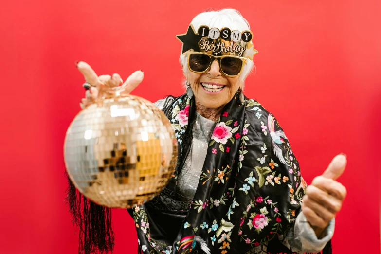 an older woman holding a disco ball and giving a thumbs up, by Julia Pishtar, pexels, photo booth, at a birthday party, sunglasses and a scarf, an elderly