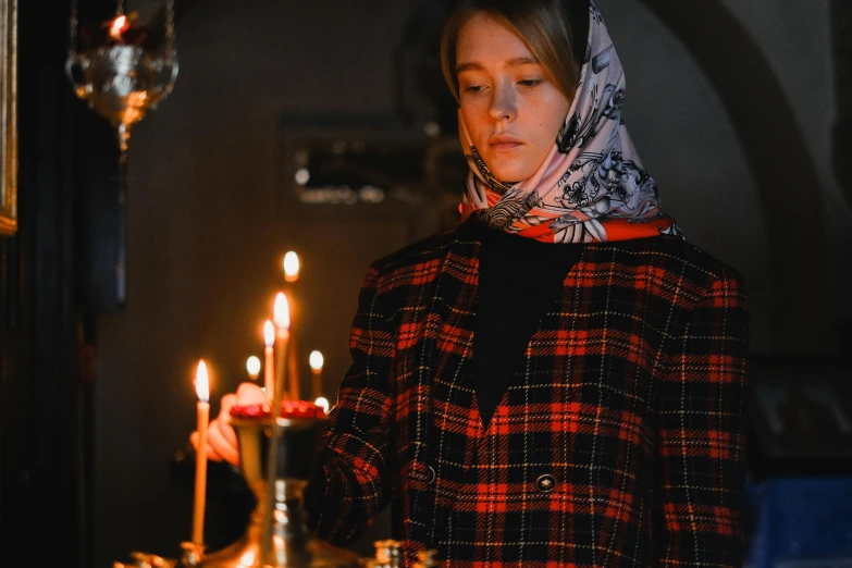 a woman standing in front of a lit candle, by Julia Pishtar, pexels contest winner, orthodox, patterned scarf, tartan vestments, scene from live action movie