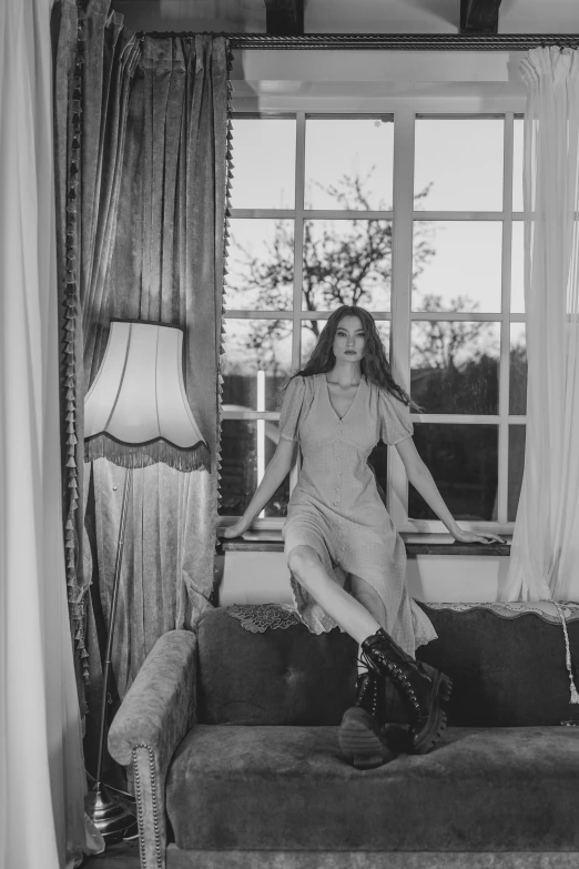 a woman sitting on a couch in front of a window, a black and white photo, inspired by Maud Naftel, unsplash, renaissance, blackpink jennie, she wears boots, album cover, evening lighting