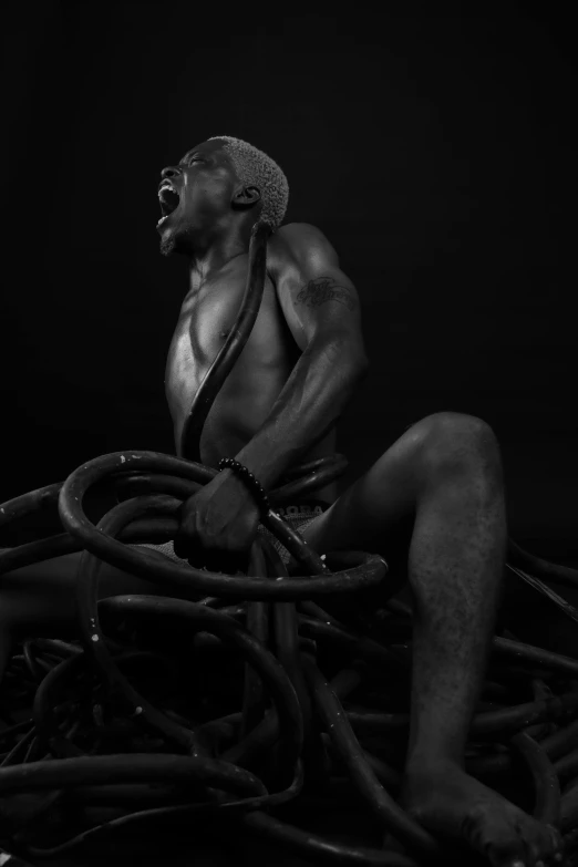 a man sitting on top of a pile of wires, an album cover, inspired by Théodore Géricault, pexels contest winner, man is with black skin, body building blacksmith, monochrome, workout