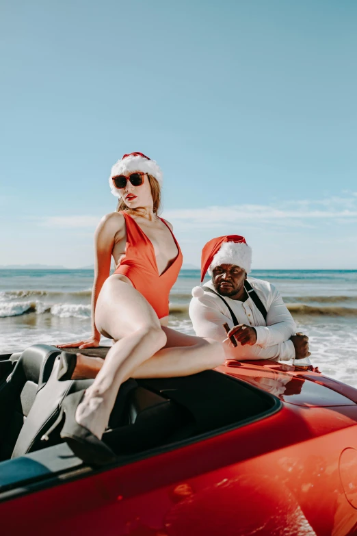 a woman sitting on top of a red car next to a man in a santa hat, in a gold one piece swimsuit, rex orange county, on ocean, mrbeast