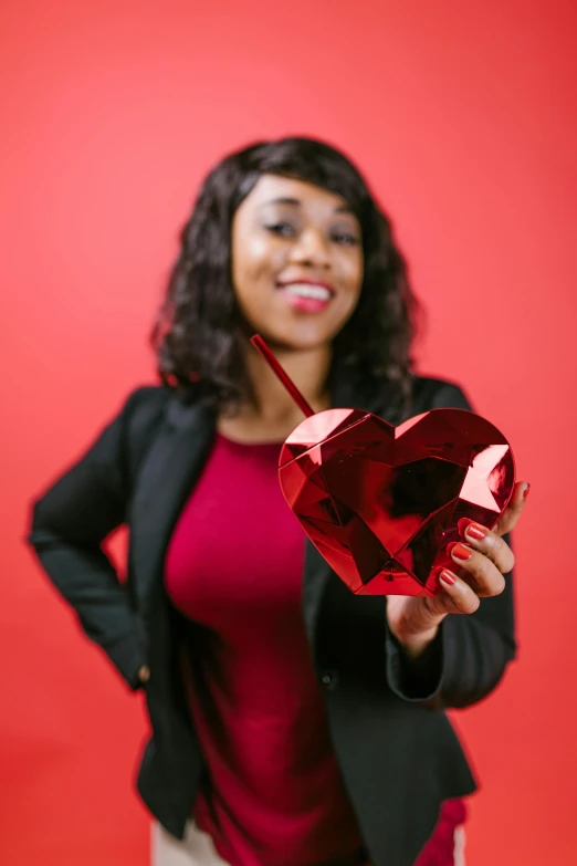 a woman holding a heart shaped object in front of a red background, by Dorothy Bradford, pexels contest winner, african american young woman, holding a staff, “diamonds, a handsome