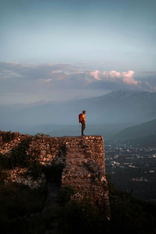 a man standing on top of a stone wall, by Alexis Grimou, happening, mountain fortress city, early evening, ruin, instagram photo