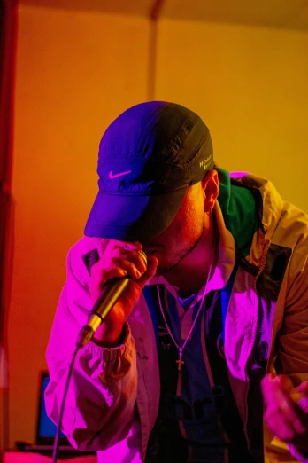 a man that is holding a microphone in his hand, an album cover, by Robbie Trevino, pexels, visual art, wearing a purple cap, sittin, glowing with colored light, college