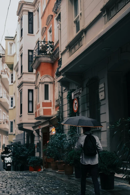 a person walking down a cobblestone street with an umbrella, by Cafer Bater, unsplash contest winner, art nouveau, istanbul, hong kong buildings, gif, gray and orange colours