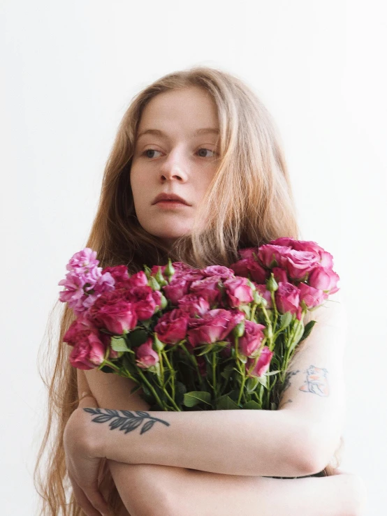 a woman holding a bunch of pink flowers, an album cover, inspired by Elsa Bleda, trending on unsplash, renaissance, sadie sink, tattoos, unhappy, mackenzie foy