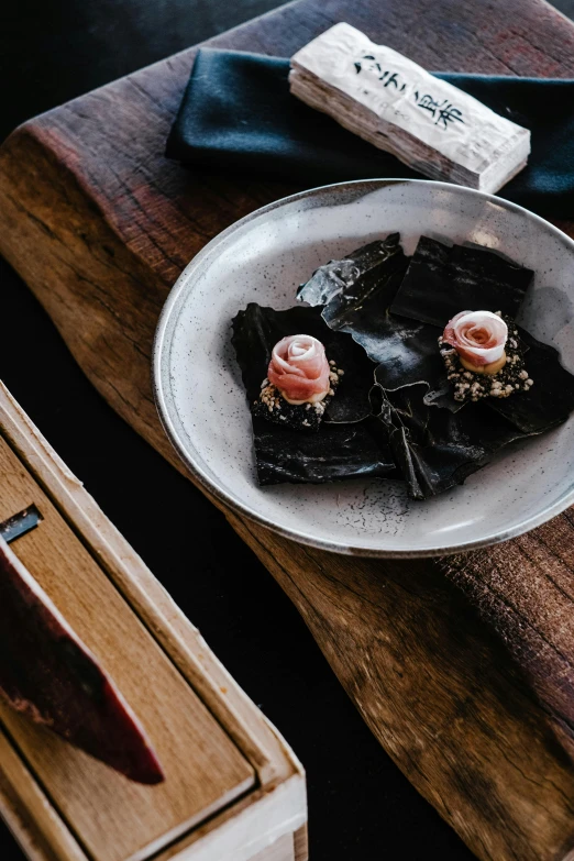 a plate of food sitting on top of a wooden table, mingei, floating kelp, wrapped in black, pink, lifestyle