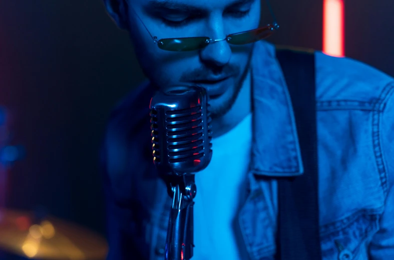 a close up of a person holding a microphone, an album cover, inspired by James Morrison, trending on pexels, photorealism, red and blue lighting, man with glasses, drinking, youtube thumbnail