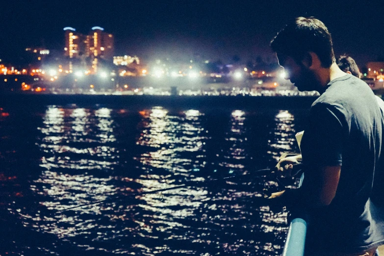 a man standing next to a body of water at night, long beach background, caio santos, fisherman, alex flores