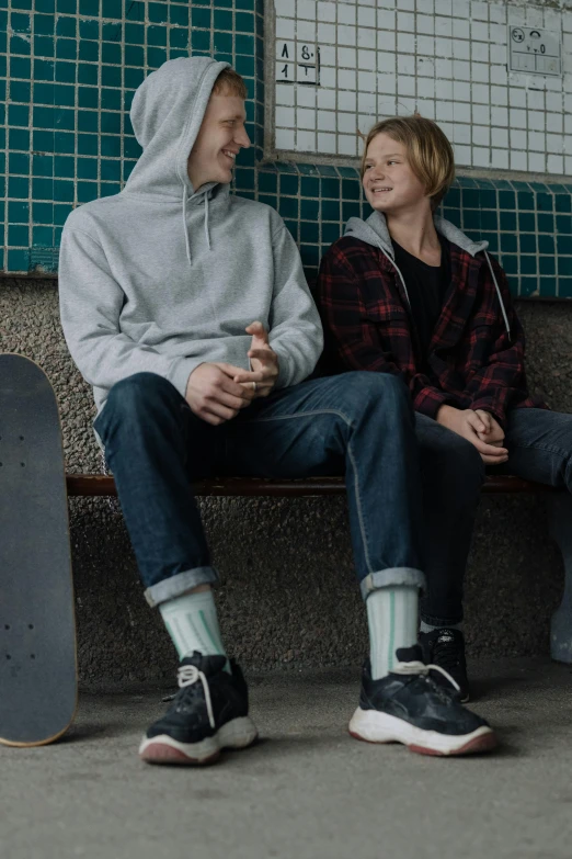 a man and a woman sitting on a bench next to a skateboard, grey hoodie, juno promotional image, full frame image, rollerskates