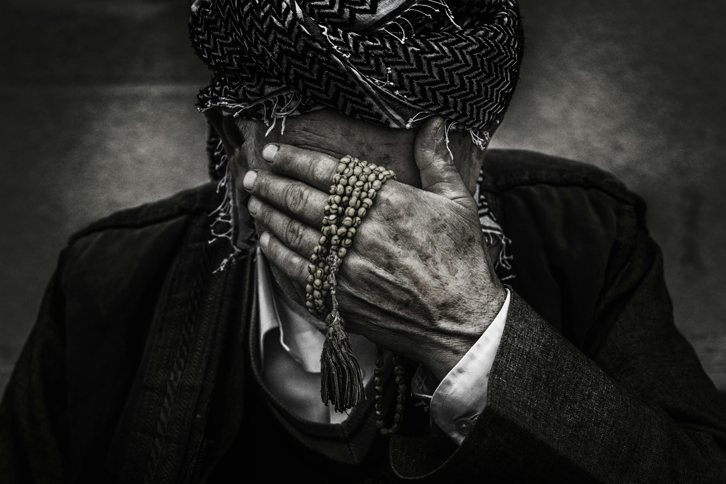 a black and white photo of a man covering his face, by Ibrahim Kodra, pexels contest winner, hyperrealism, beads, prayer, middle east, kerem beyit