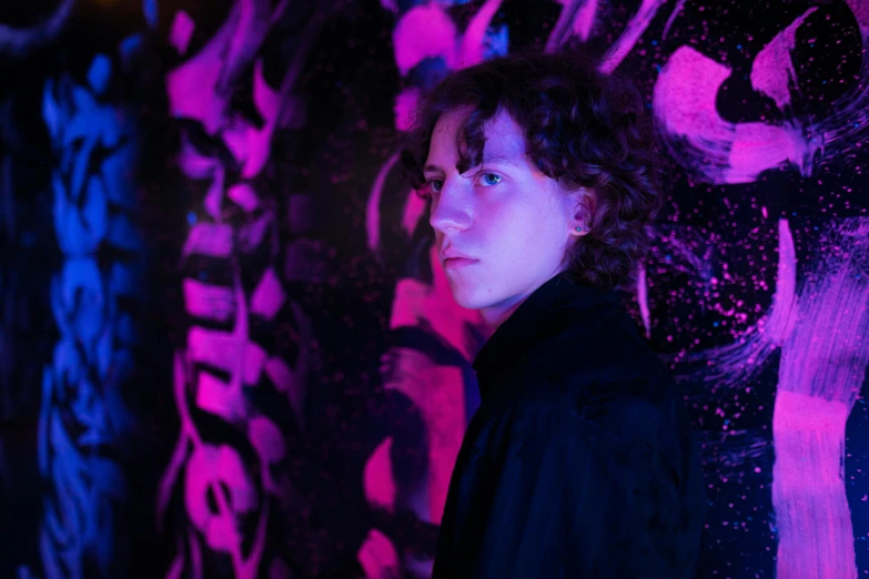 a woman standing in front of a wall covered in graffiti, an album cover, unsplash, graffiti, portrait of timothee chalamet, magenta lighting. fantasy, ignant, felix englund