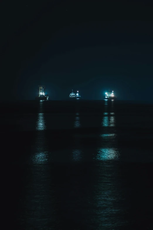 a group of boats floating on top of a body of water at night, by Adam Marczyński, pexels, minimalism, shipfleet on the horizon, headlights, cold blue light, oil rig