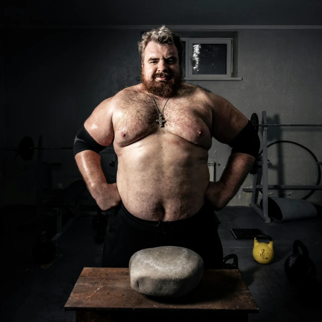 a man standing next to a rock in a gym, by Olaf Gulbransson, featured on reddit, purism, portrait of sam hyde, big stomach, sitting on top a table, heavy make up