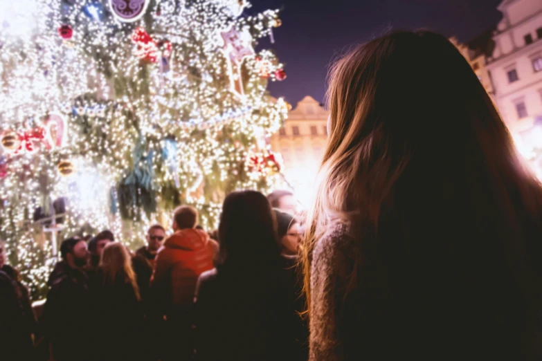 a woman standing in front of a christmas tree, a photo, happening, crowded square, instagram photo, good lighted photo, long shot from the back