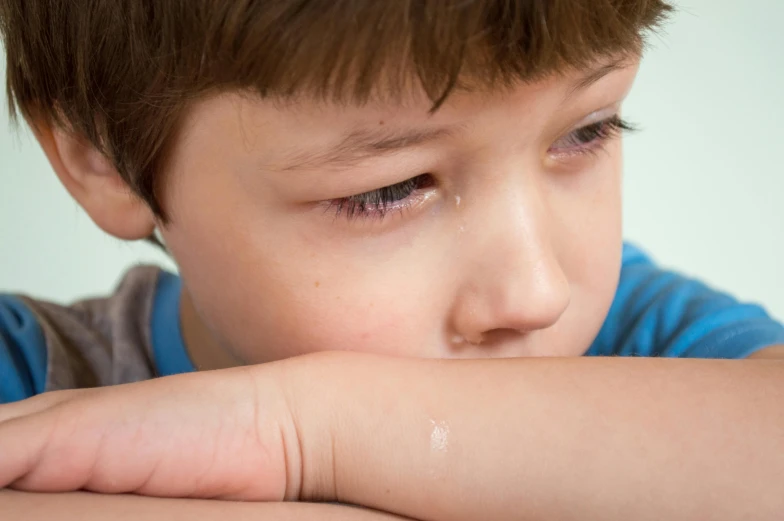 a young boy sitting at a table with his hand on his chin, a picture, trending on pexels, a close up shot of a crying eye, educational, hugging his knees, frozen tear