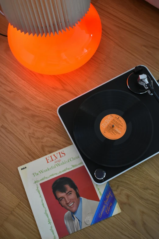 a record sitting on top of a table next to a lamp, by Doug Ohlson, electric orange glowing lights, elvis, item, high angle