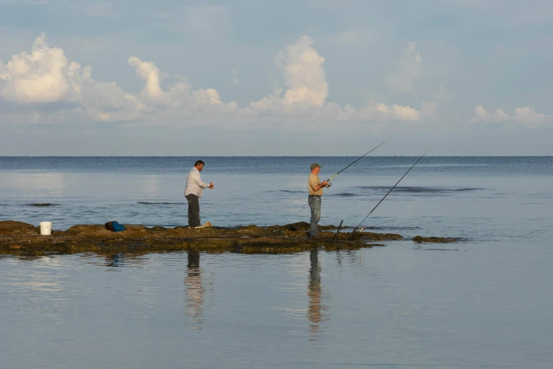 a couple of men standing on top of a rock next to the ocean, fishing pole, standing in shallow water, ray casting, manly