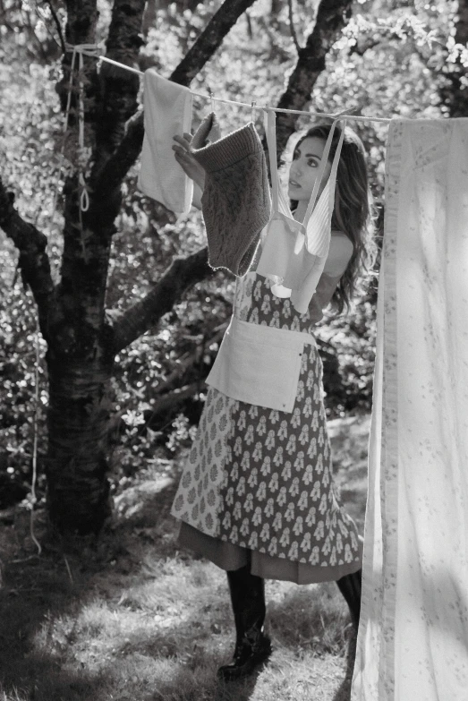 a black and white photo of a woman hanging clothes on a clothesline, inspired by Grete Stern, unsplash, renaissance, hanbok apron, next to a tree, lucy hale, at a fashion shoot