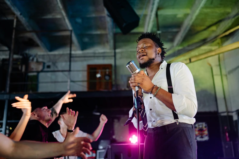 a man standing on top of a stage holding a microphone, pexels, happening, people dancing in background, emmanuel shiru, william warehouse, close to night