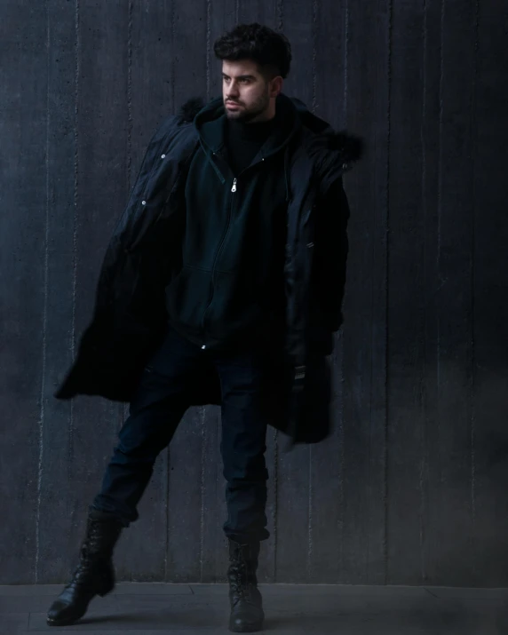 a man standing in front of a black wall, an album cover, inspired by Raphaël Collin, pexels contest winner, hurufiyya, wearing long black winter coat, zayn malik, full body:: snow outside::, prideful look