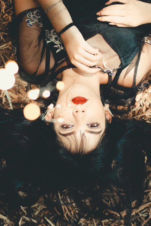 a woman laying on top of a pile of hay, inspired by Elsa Bleda, trending on pexels, dark lipstick, with haunted eyes and dark hair, fairy lights, young woman looking up