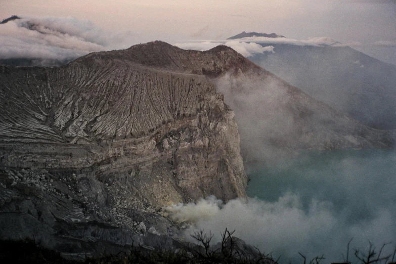 a large body of water with a mountain in the background, pexels contest winner, sumatraism, white lava, looking down a cliff, smokey atmosphere, concert