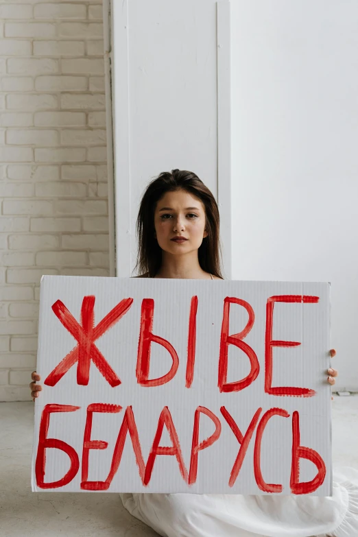 a woman sitting on the floor holding a sign, a poster, by Serhii Vasylkivsky, pexels, feminist art, okay one fear, x - day, russian, 🚿🗝📝