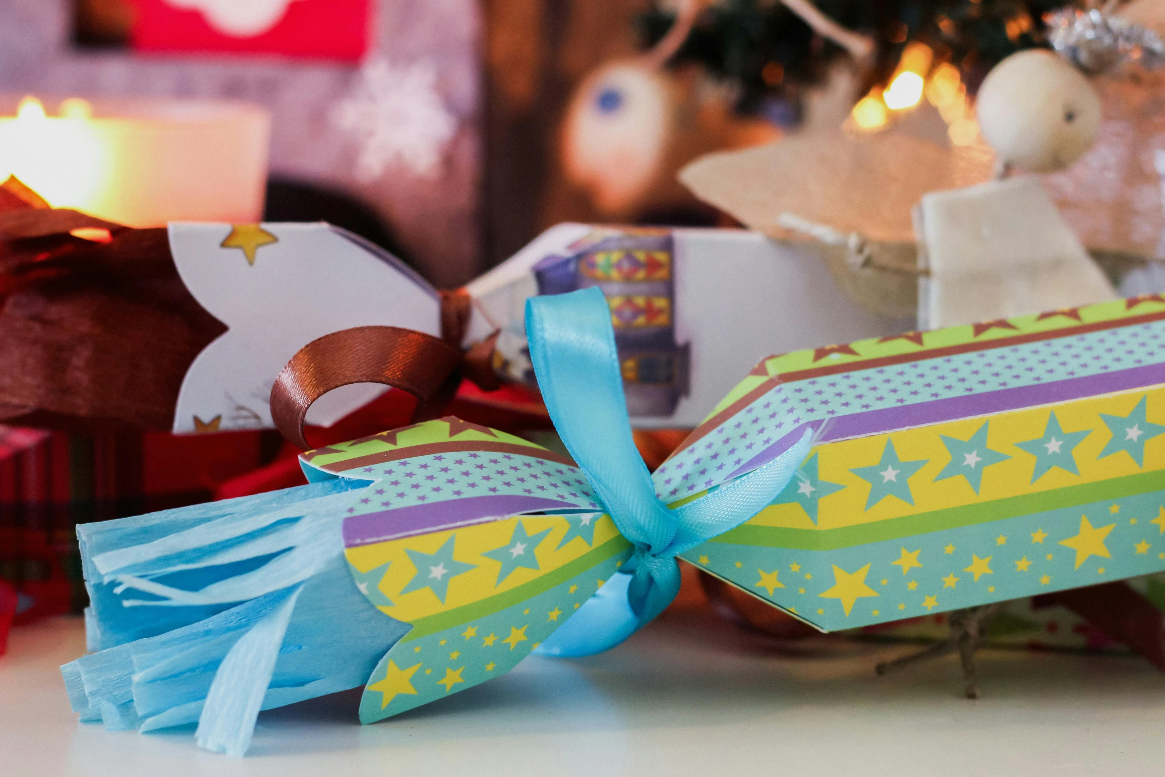 a christmas cracker sitting on top of a table next to a christmas tree, by Alice Mason, pexels contest winner, process art, blue and yellow ribbons, colorful paper lanterns, close up shot from the side, a wooden