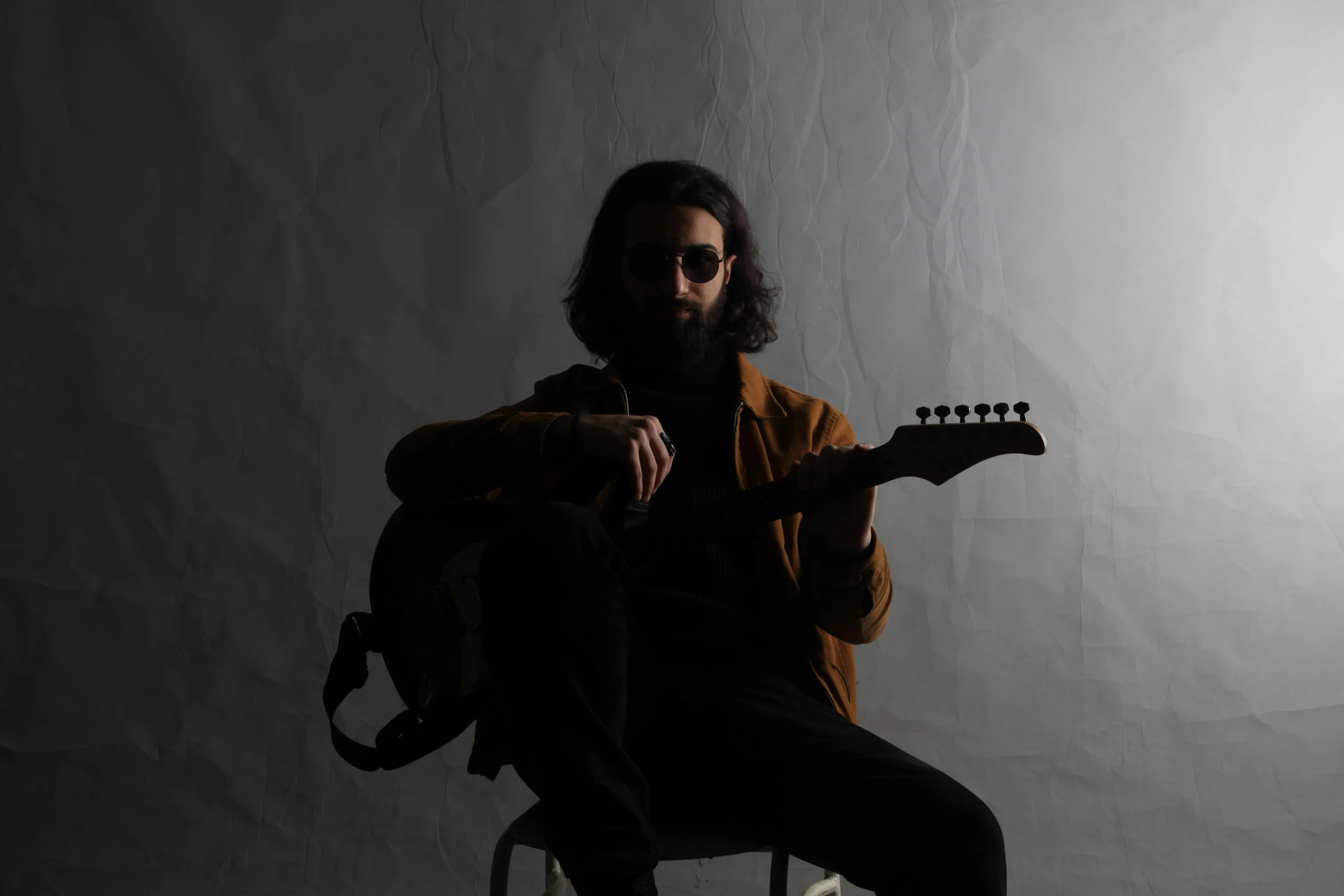 a man sitting in a chair with a guitar, kyza saleem, plain background, lit from behind, man with beard
