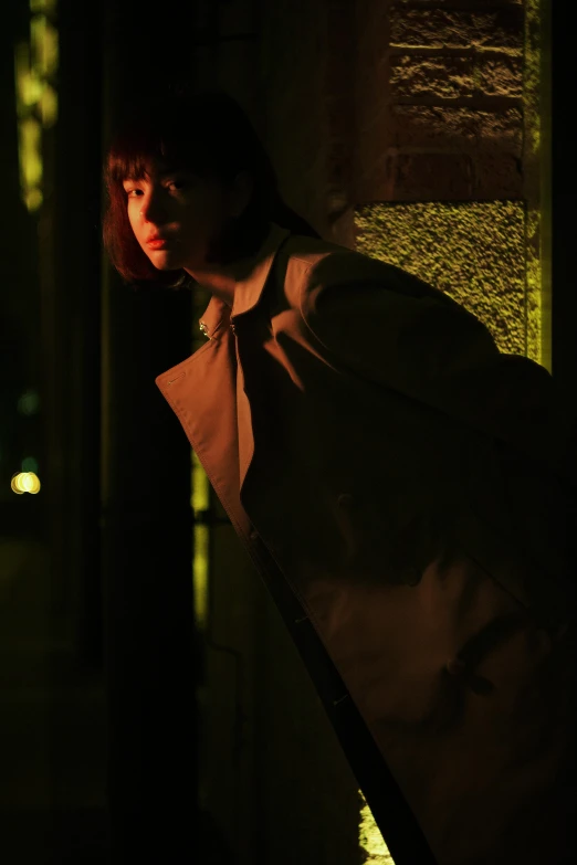 a woman leaning against a wall in the dark, an album cover, inspired by Nan Goldin, unsplash, conceptual art, he is wearing a trenchcoat, finn wolfhard, male model, nightlife