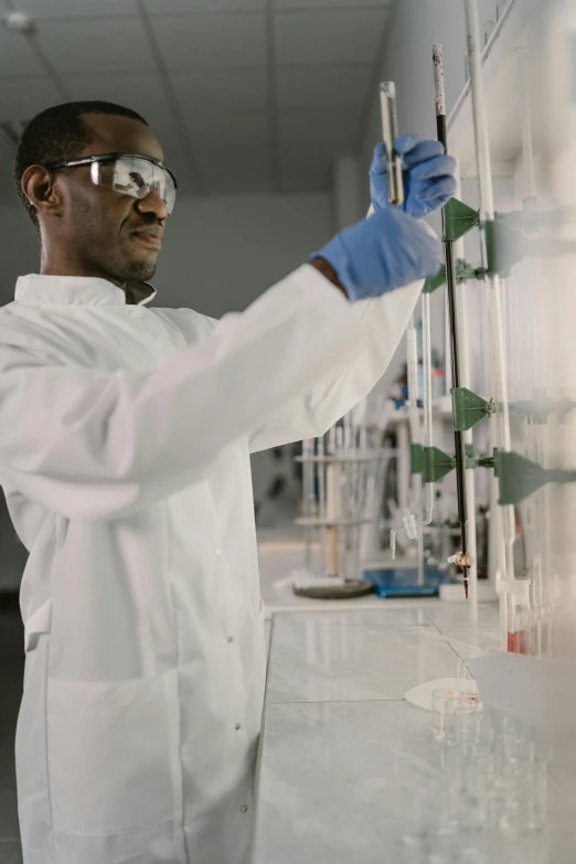 a man in a lab coat and goggles working in a laboratory, pexels, afro tech, low quality footage, promo image, wide views