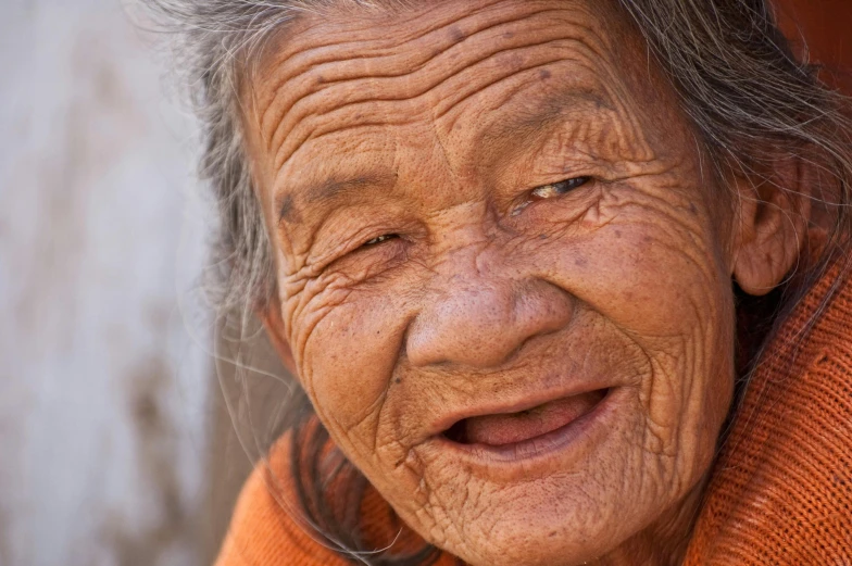 a close up of a person wearing an orange sweater, by Lee Loughridge, mingei, wrinkled face, laos, avatar image, smiling woman
