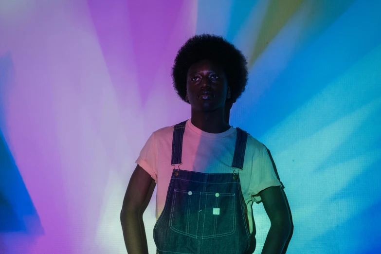 a man standing in front of a colorful light, with afro, wearing overalls, faded out colors, model posing