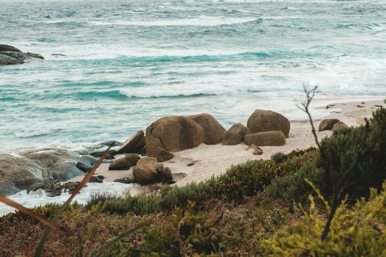 a man riding a surfboard on top of a sandy beach, by Lee Loughridge, unsplash contest winner, boulders, rocky grass field, whales showing from the waves, australian bush