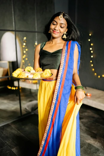 a woman standing in a room holding a plate of food, instagram, hurufiyya, blue and yellow theme, wearing festive clothing, side lights, curated collections